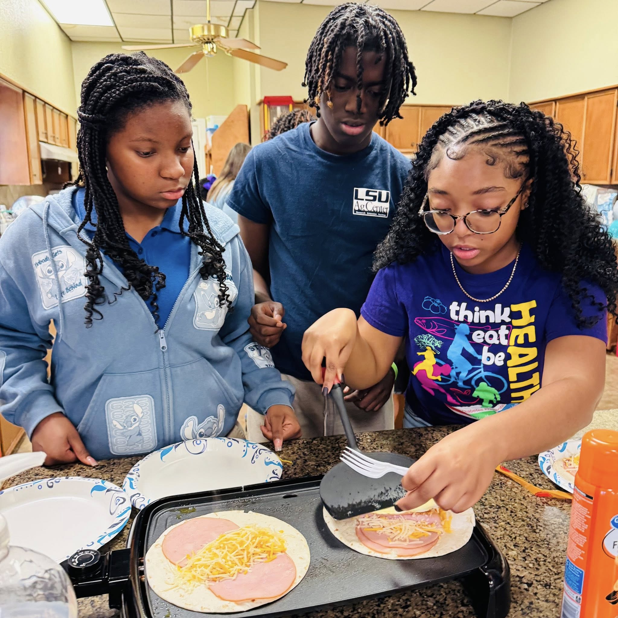 Three teens cooking on a griddle.